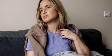 Gen Z woman looking tired sitting on her couch.